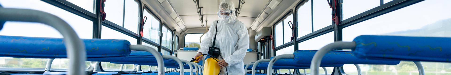 mężczyzna w kombinezonie ochronnym dezynfekuje autobus